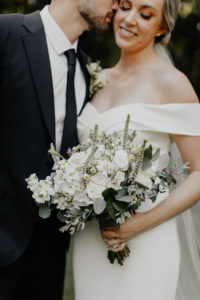 Classic Florida Bride and Groom, Bride Holding Delicate White Floral Bouquet with Greenery, Wearing Fitted Off The Shoulder BHLDN Wedding Dress, Groom in Classic Black Suit and Tie | Tampa Bay Hair and Makeup Artist Femme Akoi Beauty Studios