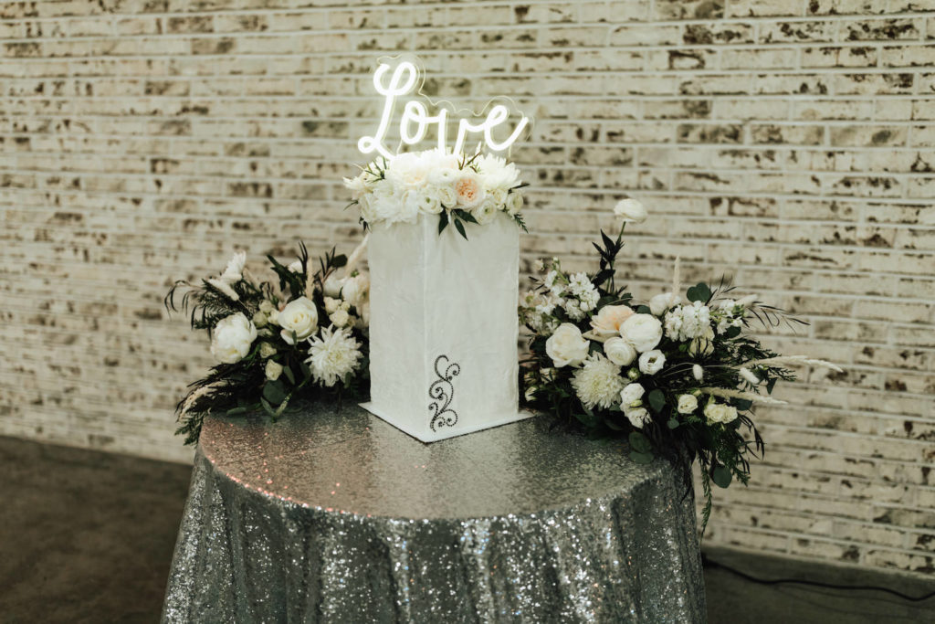 Winter Florida Sequin Sparkle Cake Table Linen with Floral Centerpieces of White Roses and Winter Pine Greenery | Tall Square Modern Unique Wedding Cake with Neon Cake Topper