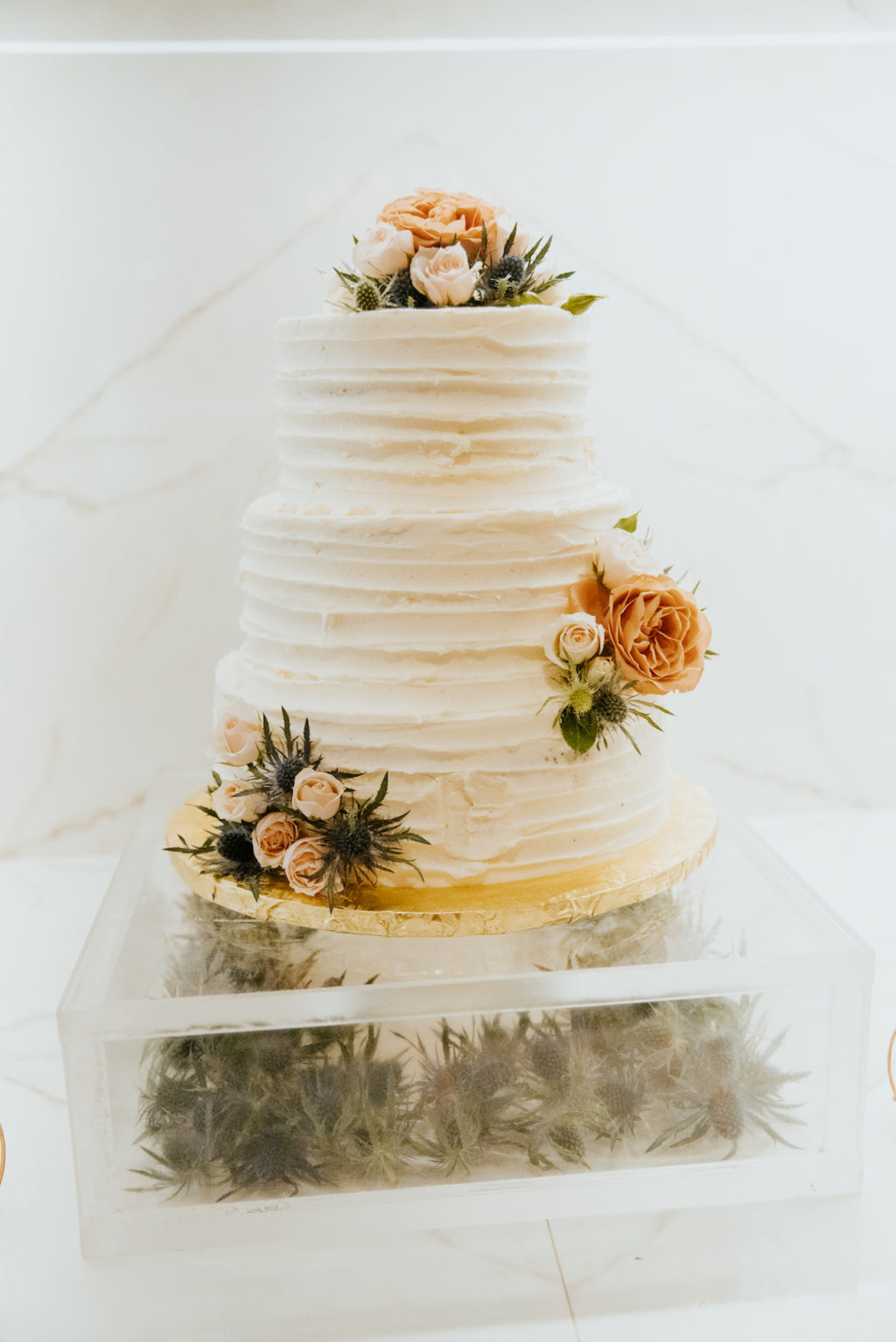 Three Tier Wedding Cake with Textured Ribbed Buttercream and Fresh Blush Pink Roses and Blue Thistle on Acrylic Clear Square Cake Stand filled with Blue Thistle
