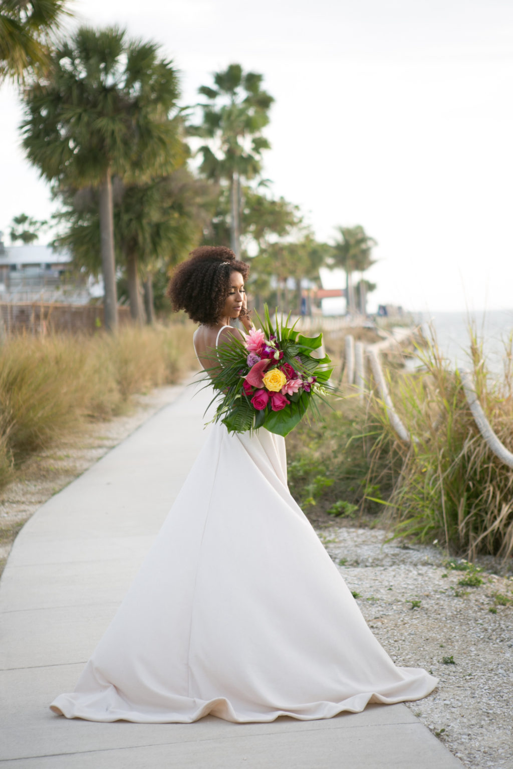 Boho Florida Bride Wearing Elegant Flowy Wedding Dress with High Slit, Holding Modern Tropical Inspired Floral Bouquet with Vibrant Yellow Roses, Bright Pink Flowers, Monstera and Palm Leaves | Salt Shack On the Bay Wedding | Tampa Bay Wedding Photographer Carrie Wildes Photography | South Tampa Wedding Planners Socialite Events | Wedding Dress Boutique Truly Forever Bridal Tampa