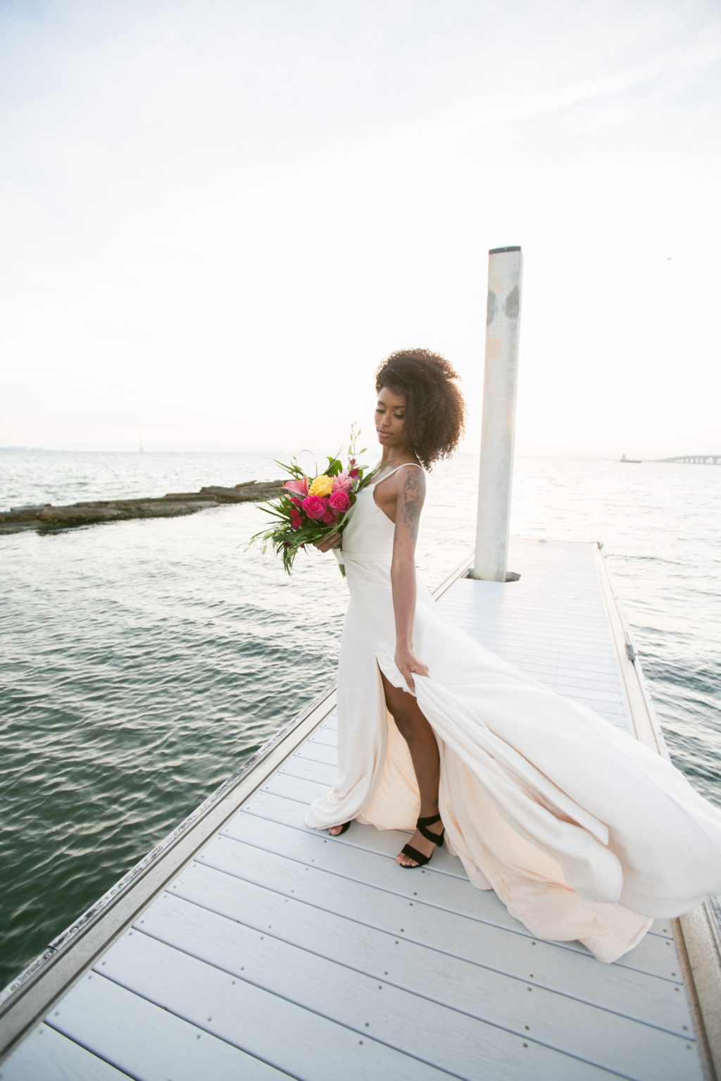 Modern Tropical Inspired Florida Bride, On Waterfront Pier in Boho Off-White Dress with High Slip, Holding Vibrant Bridal Bouquet