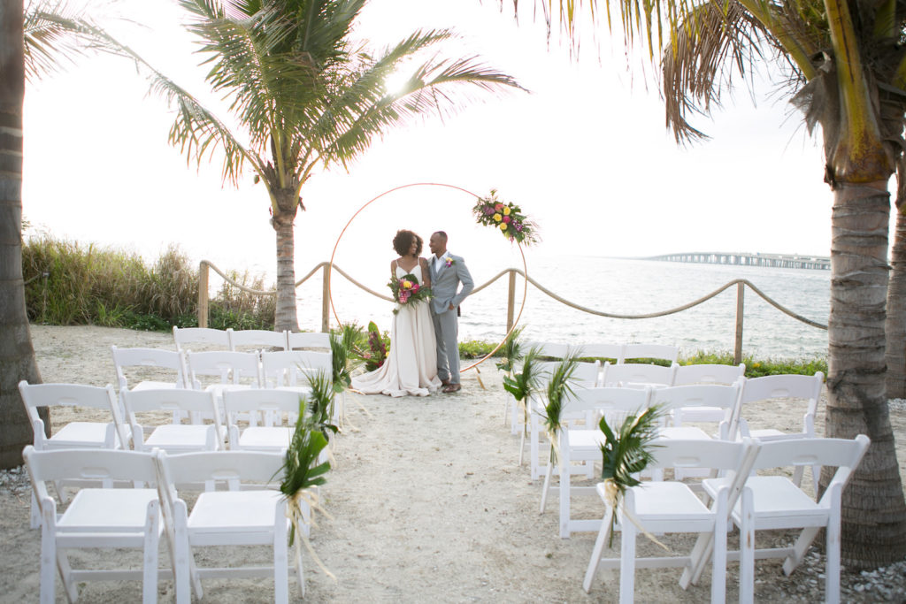 Modern Tropical Inspired Florida Bride and Groom, On Waterfront Pier in Boho Off-White Dress with High Slip, Holding Vibrant Bridal Bouquet | Salt Shack On the Bay Wedding Styled Shoot | Tampa Bay Wedding Photographer Carrie Wildes Photography | South Tampa Wedding Planner Socialite Events