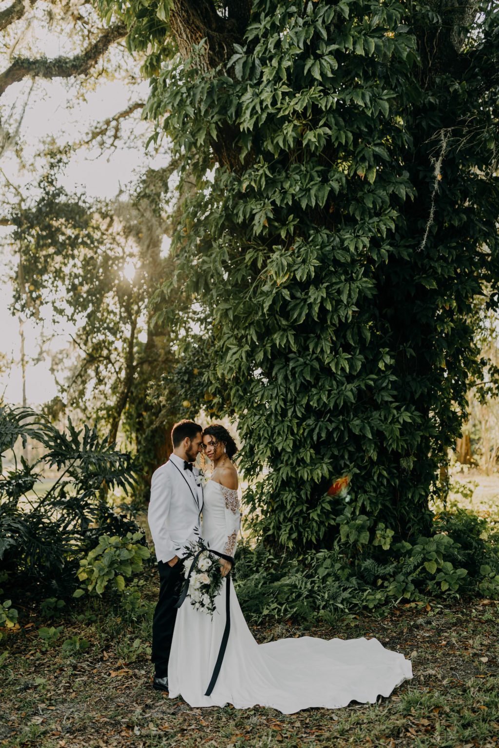 Outdoor Bride and Groom Portrait | Groom Wearing Classic Formal White Jacket with Black Lapel and Bow Tie | Off the Shoulder Lace Sleeve Sheath Wedding Gown Bridal Dress | Amber McWhorter Photography