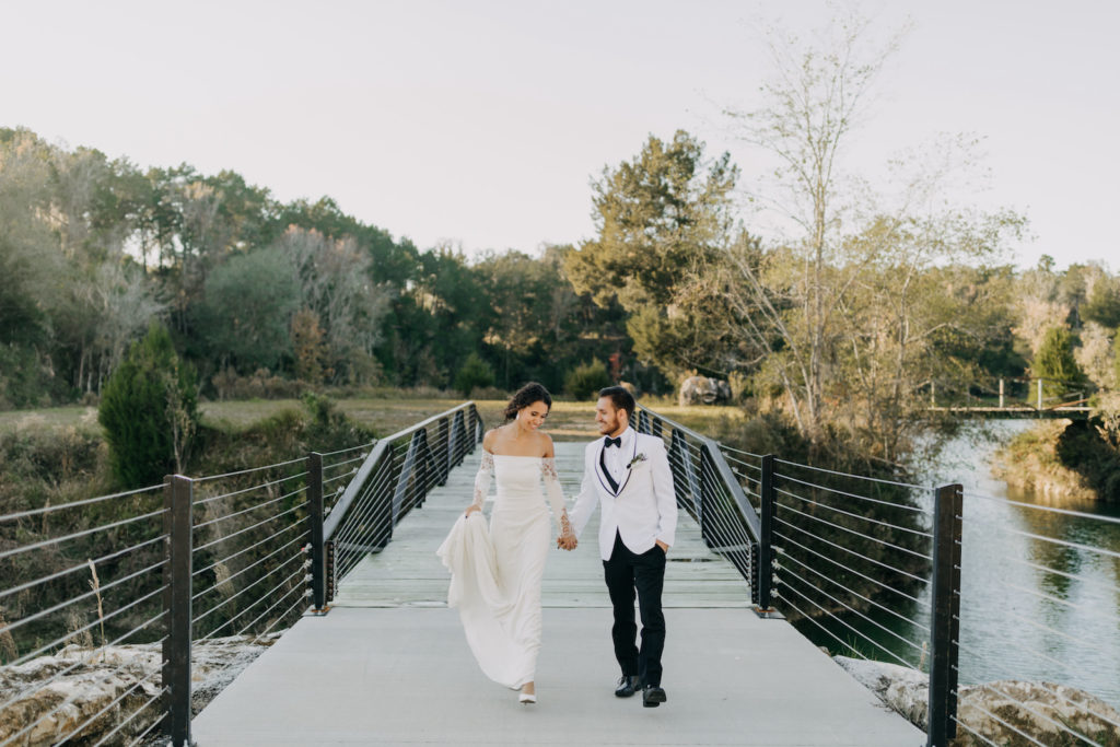 Waterfront Outdoor Bride and Groom Portrait on Bridge over Stream | Groom Wearing Classic Formal White Jacket with Black Lapel and Bow Tie | Off the Shoulder Lace Sleeve Sheath Wedding Gown Bridal Dress | Amber McWhorter Photography