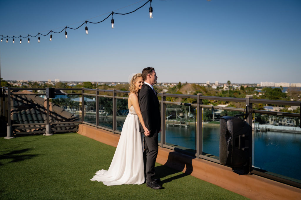 Romantic Intimate Bride Holding Hands with Groom from Behind on Rooftop Waterfront St. Pete Wedding Venue Hotel Zamora | Tampa Wedding Dress Isabel O'Neil Bridal | First Touch Wedding Portrait