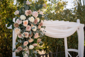 Mauve, Blush Pink, Ivory Roses and Eucalyptus Greenery Floral Arrangement on White Pergola Style Arch with Linen Draping | Tampa Bay Wedding Florist Iza's Flowers