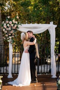 Florida Bride and Groom Exchanging Wedding Vows During Outdoor Courtyard Ceremony, White Pergola Style Arch with Linen Draping, Mauve and Ivory Roses, Eucalyptus Greenery Floral Arrangement | St. Pete Wedding Venue Hotel Zamora | Tampa Wedding Florist Iza's Flowers