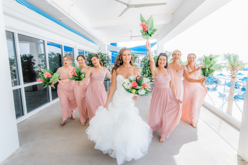 Tampa Bay Bride in Strapless Sweetheart Mermaid Beaded and Lace Wedding Dress with Organza Ruffle Skirt Holding Tropical Floral Bouquet and Bridesmaids in Pink Mix and Match Dresses | Wedding Venue Hilton Clearwater Beach | Wedding Florist Iza's Flowers