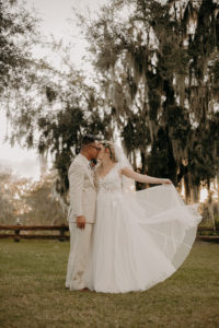 Romantic Rustic Bride Holding Tulle Skirt of Flowy A-Line Wedding Dress and Groom Sunset Wedding Portrait | Plant City Wedding Venue Florida Rustic Barn Weddings
