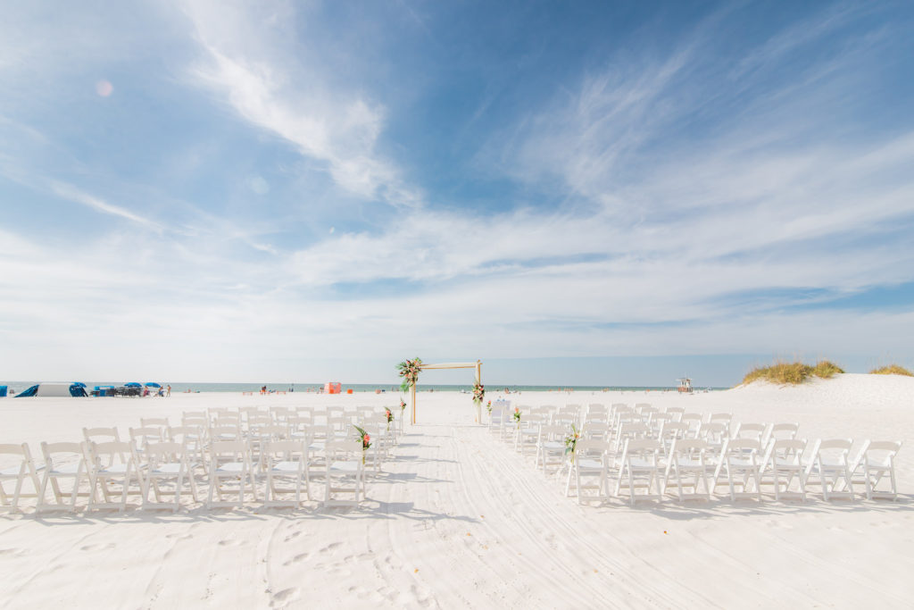 Tropical Wedding Ceremony Decor on the Beach, Bamboo Arch with Colorful Floral Arrangements, White Folding Chairs | Wedding Venue Hilton Clearwater Beach