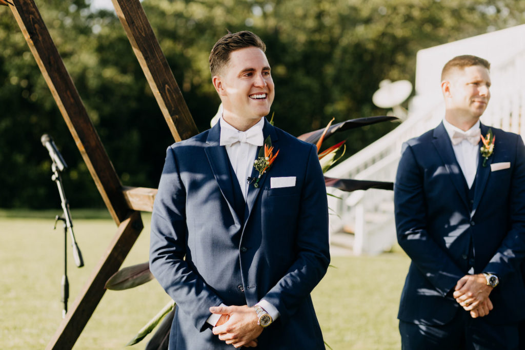 Florida Groom in Blue Suit and White Bowtie with Birds of Paradise Flower Boutonniere Reaction to Bride Walking Down the Wedding Ceremony Aisle | Tampa Bay Wedding Photographer Amber McWhorter Photography