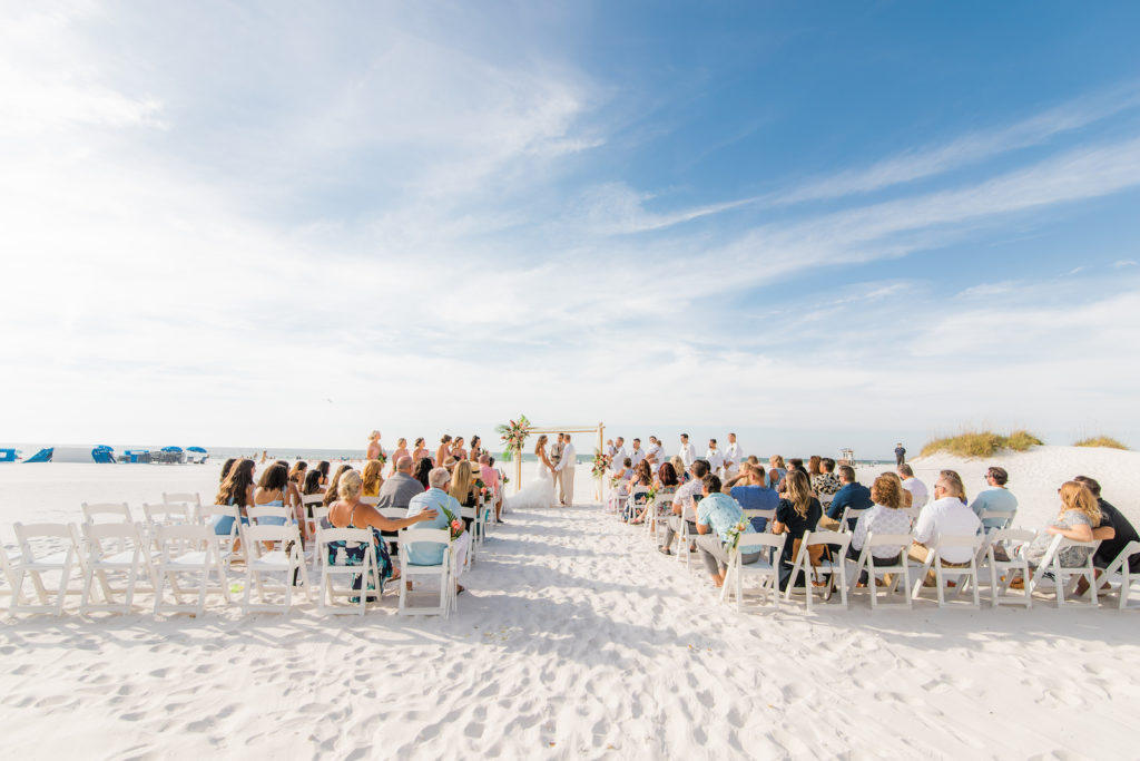 Tropical Wedding Ceremony Decor on the Beach, Bamboo Arch with Colorful Floral Arrangements, White Folding Chairs | Wedding Venue Hilton Clearwater Beach