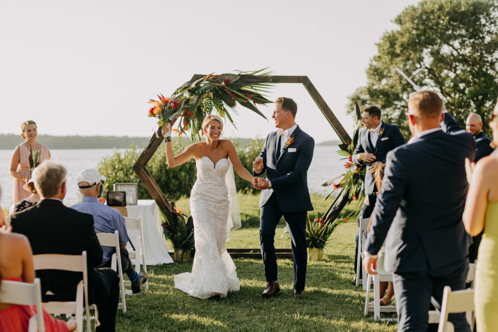 Tropical Elegant Bride and Groom Exchanging Wedding Ceremony Vows, Wooden Geometric Arch with Tropical Floral Arrangement | Tampa Bay Wedding Photographer Amber McWhorter Photography | Waterfront Wedding Venue Tampa Bay Watch
