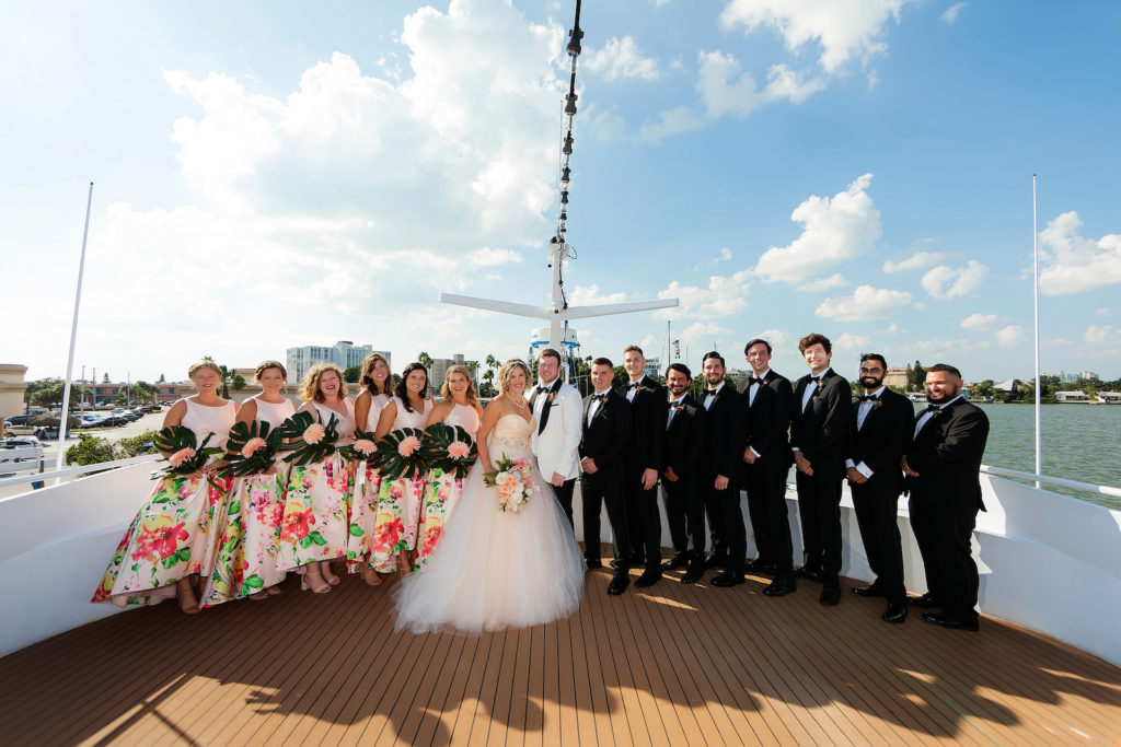 Florida Bride in Strapless Tulle Skirt Ballgown Blush Pink Lining Wedding Dress, Groom in White Tuxedo, Bridesmaids Wearing Tropical Pink and Floral Skirt Matching Dresses Holding Monstera Leaf and Pink Flower Bouquets, Groomsmen in Black Tuxedos, Wedding Party on Waterfront Wedding Venue Yacht StarShip | Tampa Bay Wedding Photographer Limelight Photography