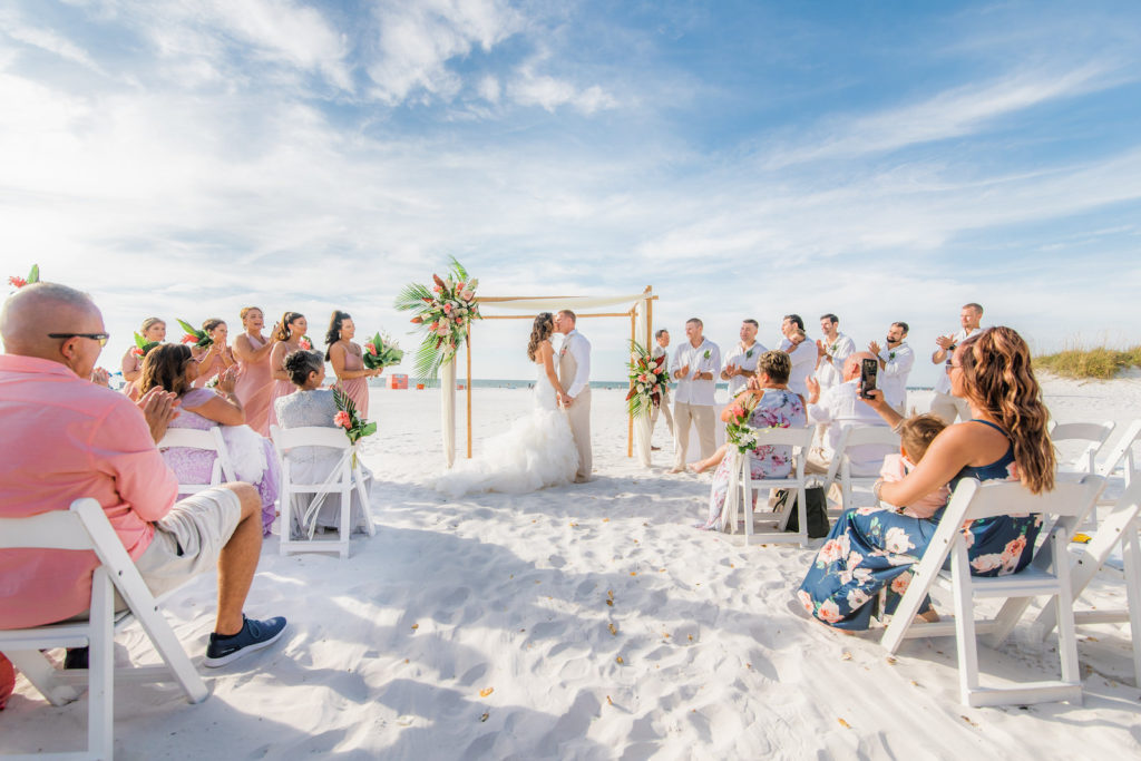 Bride and Groom Exchange Kiss During Tropical Wedding Ceremony Under Bamboo Arch on Beach | Wedding Venue Hilton Clearwater Beach
