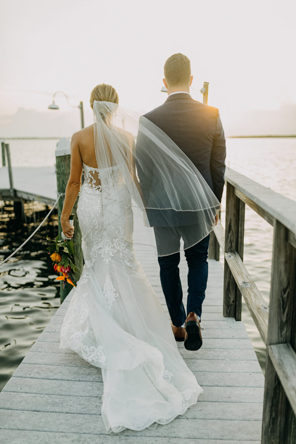 Florida Bride in Lace and Illusion Stella York Wedding Dress and Groom Walking on Pier During Sunset | Tampa Bay Wedding Photographer Amber McWhorter Photography