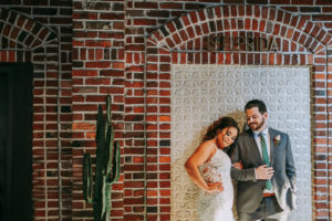 Historic Venue Brick Wall Backdrop Bride and Groom Portrait at Downtown St. Pete Wedding Venue Red Mesa Events | Groom Wearing Classic Charcoal Grey Suit with Green Tie | Perfecting the Plan