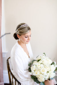 Classic Bride with Hair in Bun and Rhinestone Headband Getting Wedding Ready in White Robe Holding White Roses Floral Bouquet | Tampa Bay Wedding Photographer Lifelong Photography Studio