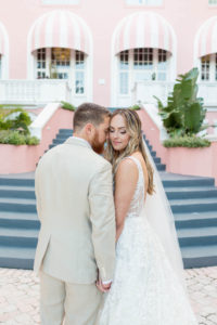 Bride and Groom Outdoor Portrait Staircase at St. Pete Beach Wedding Venue The Don CeSar Pink Palace | Monique Lhuillier Designer Wedding Dress A Line Ballgown Lace Bridal Gown | Groom Wearing Casual Khaki Suite