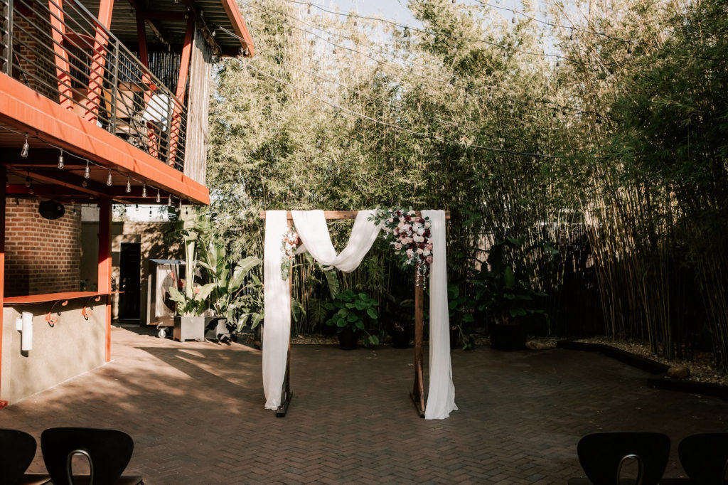 Industrial Inspired Florida Wedding in Bamboo Garden Courtyard, Decorated with Romantic Moody Florals, Ceremony Arch with Soft White Draping, Pink, Red, White and Burgundy Roses with Eucalyptus Greenery | Tampa Bay's Best Place for a Wedding NOVA 535 in Downtown St. Pete