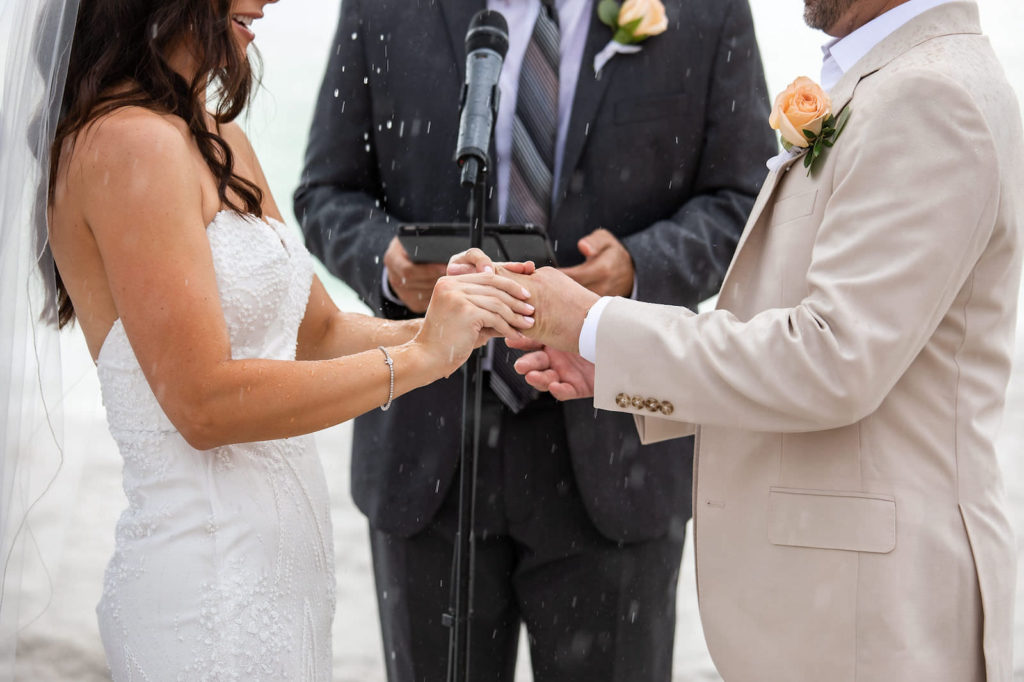 Bride and Groom Exchanging Rings during Ceremony Rain Storm | Bride Wearing Strapless Sheath Wedding Gown by Tara Keilly | Groom Wearing Casual Khaki Suit