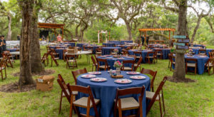 DIY Backyard Tampa Bay Wedding Reception Decor, Round Tables with Navy Blue Table Linens, Mahogany Folding Chairs, Low Floral Centerpieces