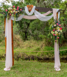 Backyard DIY Tampa Wedding Ceremony Decor, Arch with White and Blush Pink Linen Draping, Colorful Pink, Blue, White with Hanging Amaranthus Floral Arrangements