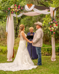 Tampa Intimate DIY Backyard Wedding Ceremony, Groom in Jeans and Tan Suit Jacket, Cowboy Hat Watching Emotional Reaction to Bride, Wooden Arch with Blush Pink and White Linen Draping, Colorful Pink, White and Blue with Greenery Floral Arrangements