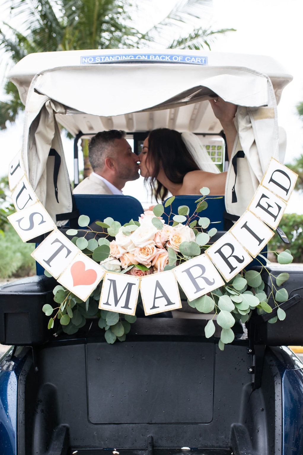 Bride and Groom Getaway Send off Classic Car Portrait Photo with Just Married Sign and Bumper Floral Arrangement with Peach Roses and Eucalyptus Greenery