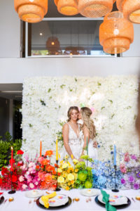 Modern Rainbow Gay LGBTQ+ Pride Wedding Reception Decor, Lesbian Brides Kissing, White Flower Wall Backdrop and Neon Sign, Red, Pink, Orange, Yellow, Green, Blue Indigo, Purple Long Flower Centerpiece and Candlesticks | Tampa Bay Wedding Planner Stephany Perry Events | Wedding Venue Hotel Alba Tampa
