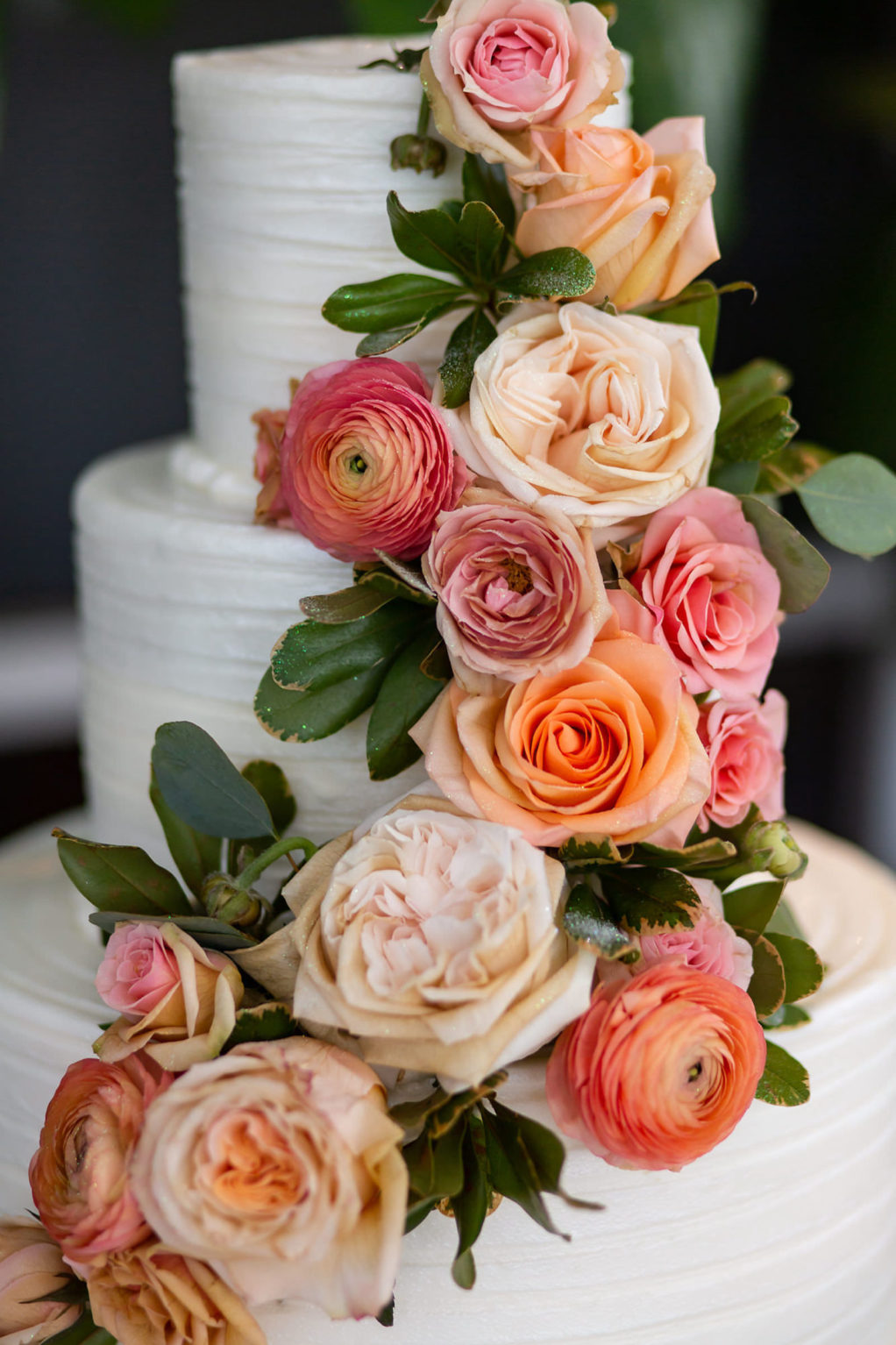 Three Tier Buttercream Striped Icing Wedding Cake with Fresh Flowers of Peach Roses and Coral Ranunculus and Greenery Cascading down the Side