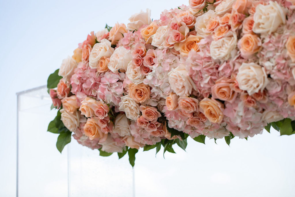 Sarasota Florida Beach Wedding Ceremony Backdrop with Clear Acrylic Arch and Floral Arrangement of Peach Pink and Coral Roses