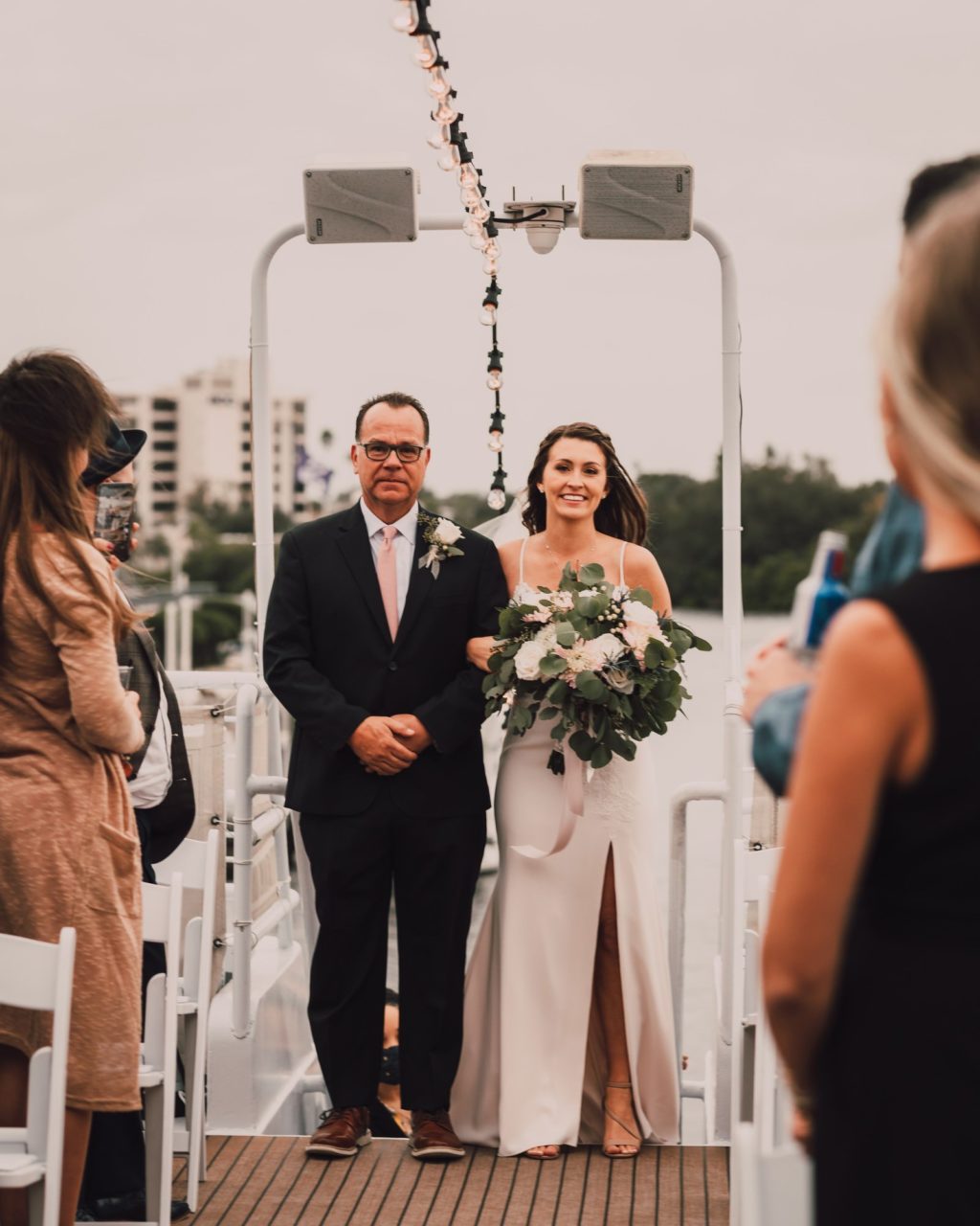 Minimalistic Bride Walking Down the Wedding Ceremony Aisle Processional with Father Holding Wild Eucalyptus Greenery and White Floral Bouquet | Tampa Bay Wedding Photographer and Videographer Bonnie Newman Creative | Wedding Hair and Makeup Femme Akoi Beauty Studio | Unique Waterfront Wedding Venue Yacht StarShip