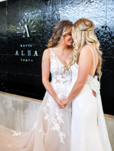 Gay LGBTQ+ Pride Wedding, Lesbian Brides in Floral Applique Lace, Illusion and Tulle Off White Plunging V Neckline Wedding Dress, Fitted Spaghetti Strap Open Back with Bow Wedding Dress | Tampa Bay Wedding Venue Hotel Alba