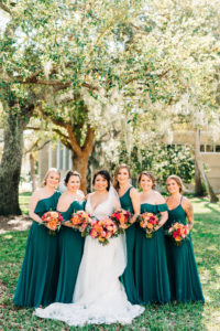 Classic Bride and Bridesmaids Outdoors in Mix and Match in Emerald Green Dresses Holding Vibrant Colorful Pink, Orange and Red Floral Bouquets | Wedding Venue Tampa Garden Club | Tampa Bay Wedding Florist Monarch Events and Design