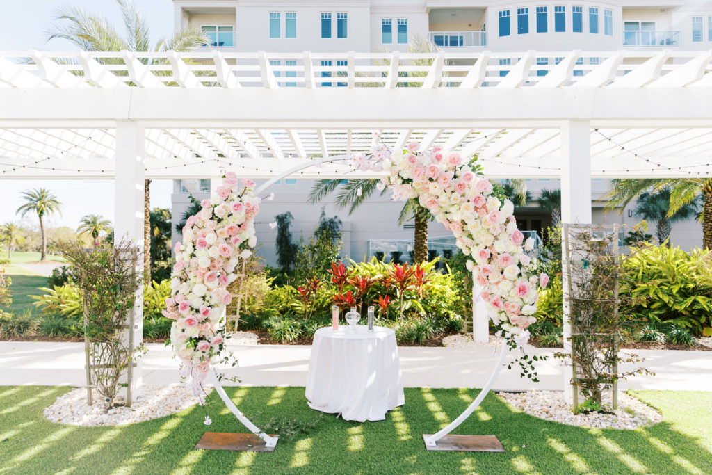 Elegant Outdoor Clearwater Lawn Wedding Ceremony and Decor at Belleview Inn, Large Floral Circle Arch Under Pergola, with Pink Cherry Blossoms, Ivory Roses, Blush Peonies, and White Hydrangeas, White Linnen Unity Table with Pink and Black Pouring Sand | Florida Luxury Wedding Planner Parties A'La Carte | Tampa Bay Wedding Florist Bruce Wayne Florals