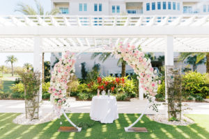 Elegant Outdoor Clearwater Lawn Wedding Ceremony and Decor at Belleview Inn, Large Floral Circle Arch Under Pergola, with Pink Cherry Blossoms, Ivory Roses, Blush Peonies, and White Hydrangeas, White Linnen Unity Table with Pink and Black Pouring Sand | Florida Luxury Wedding Planner Parties A'La Carte | Tampa Bay Wedding Florist Bruce Wayne Florals