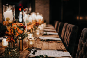 Dark and Moody Wedding Reception Decor, Long Wooden Feasting Table, Black Tufted Chairs, Candlesticks, Burnt Orange Florals | Wedding Venue Urban Stillhouse St. Pete