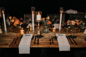 Dark and Moody Wedding Reception Decor, White Linen Napkins with Laser Cut Table Place Cards, Paper Menus, Black Silverware, Long Wooden Feasting Table, Black Tufted Chairs, Candlesticks, Burnt Orange Florals | Wedding Venue and Caterer Urban Stillhouse St. Pete