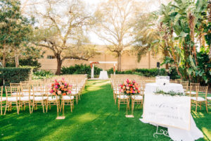 Outdoor Garden Wedding Ceremony Decor, Gold Chiavari Chairs, White Pergola, Vibrant and Colorful Pink, Orange and Red Floral Arrangements on Gold Geometric Stands, White Welcome Sign in Gold Frame with Greenery Garland | Wedding Venue Tampa Garden Club | Wedding Florist Monarch Events and Design | Wedding Rentals Kate Ryan Event Rentals