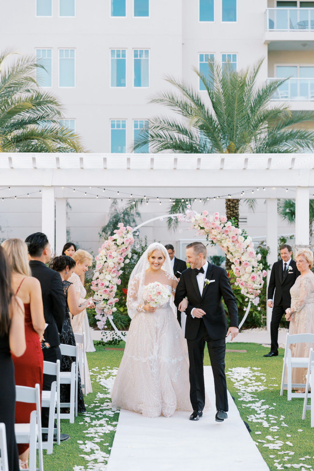 Bride and Groom Just Married Wedding Recessional During Elegant Outdoor Clearwater Lawn Ceremon at Belleview Inn, Garden Inspired Decor with Large Floral Circle Arch Under Pergola, with Pink Cherry Blossoms, Ivory Roses, Blush Peonies, and White Hydrangeas, Bride Wearing Adam Zhoar A Line Wedding Dress, Groom in Classic Black Giorgio Armani Tux | Florida Luxury Wedding Planner Parties A'La Carte | Tampa Bay Wedding Florist Bruce Wayne Florals | South Tampa Bridal Boutique Isabel O'Neil Bridal Collection