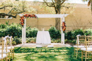 Garden Outdoor Wedding Ceremony Decor, White Pergola with Lush Vibrant and Colorful Floral Arrangements, Greenery, Pink, Orange, Red and Purple Flowers, Gold Chiavari Chairs | Wedding Venue Tampa Garden Club | Wedding Florist Monarch Events and Design | Wedding Rentals Kate Ryan Event Rentals