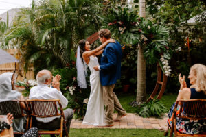 Tampa Bay Bride and Groom Exchange Vows in Backyard Ceremony, Tropical Outdoor Wedding Decor, Circle Arch with Monstera Leaf Greenery and White Orchids, Bamboo Folding Chair Rentals | Florida Wedding Planner Parties A'La Carte