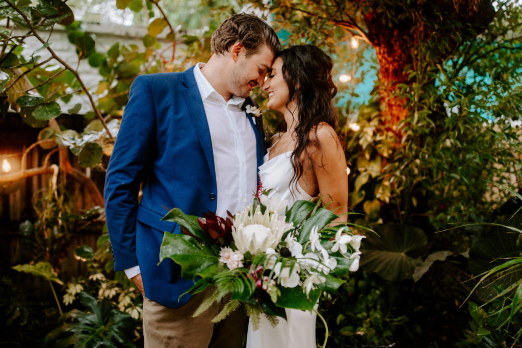 St. Petersburg Bride and Groom At Backyard Wedding Ceremony, Tropical Inspired Florida Bridal Bouquet, White King Protea with Red Florals and Orchids, Monstera Leafs, Palm Greenery, Jungle Inspired Wedding | Tampa Bay Wedding Planner Parties A'La Carte