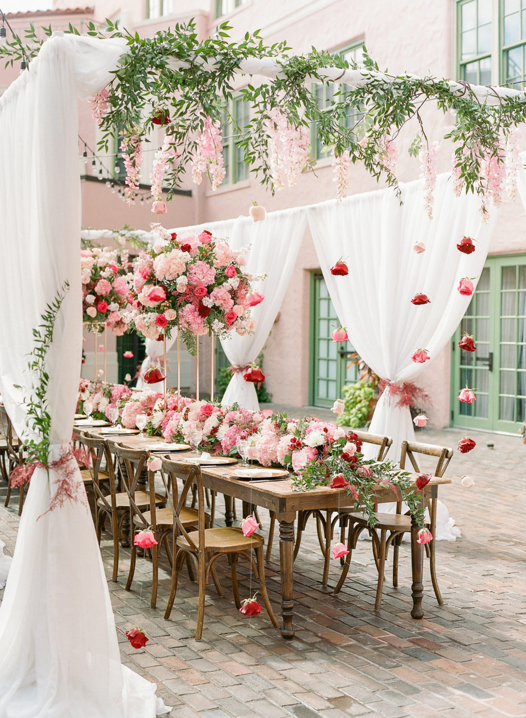 Elegant Garden Theme Wedding Reception Decor, White Drapery with Hanging Pink Flowers, Long Wooden Feasting Table with Wooden Cross Back Chairs, Tall Pink, Ivory and Red Floral Centerpiece | St. Pete Wedding Venue The Vinoy Renaissance