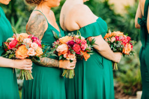 Outdoor Garden Wedding Ceremony, Bridesmaids in Mix and Match Emerald Green Dresses Holding Vibrant Colorful Floral Bouquets, Red, Pink and Orange Roses with Greenery | Tampa Bay Wedding Florist Monarch Events and Design