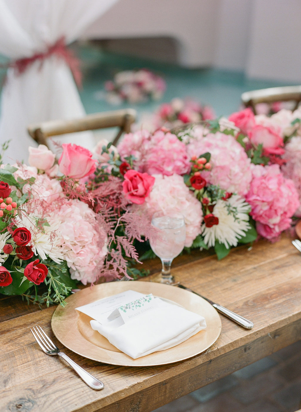 Elegant Garden Themed Wedding Reception Decor, Long Wooden Feasting Table with Gold Chargers and White Linen Napkins, Pink Hydrangeas and Roses with White Flowers and Greenery Lush Table Runner