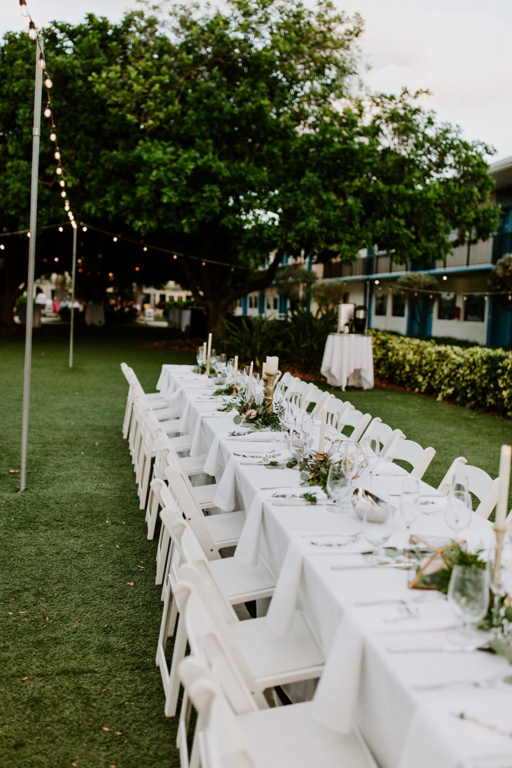 Garden Tropical Wedding Reception Decor, Long Feasting Table with White Linens, Greenery Floral Centerpieces, Candlesticks | St. Pete Wedding Venue Postcard Inn on the Beach