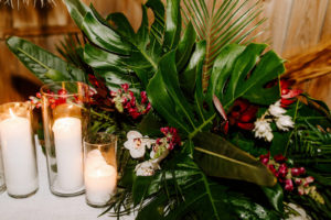 Jungle Inspired Wedding Decor, Low Floral Centerpieces with Tropical Monstera and Palm Leaf Greenery and Bright Pink and Red Florals with White Orchids, Candles | Florida Wedding Planner Parties A'La Carte
