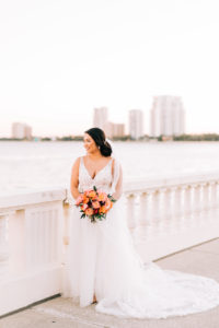 Tampa Bay Bride in Classic Lace Plunging V Neckline Tule A-Line Wedding Dress Holding Vibrant Colorful Orange and Pink Floral Bouquet